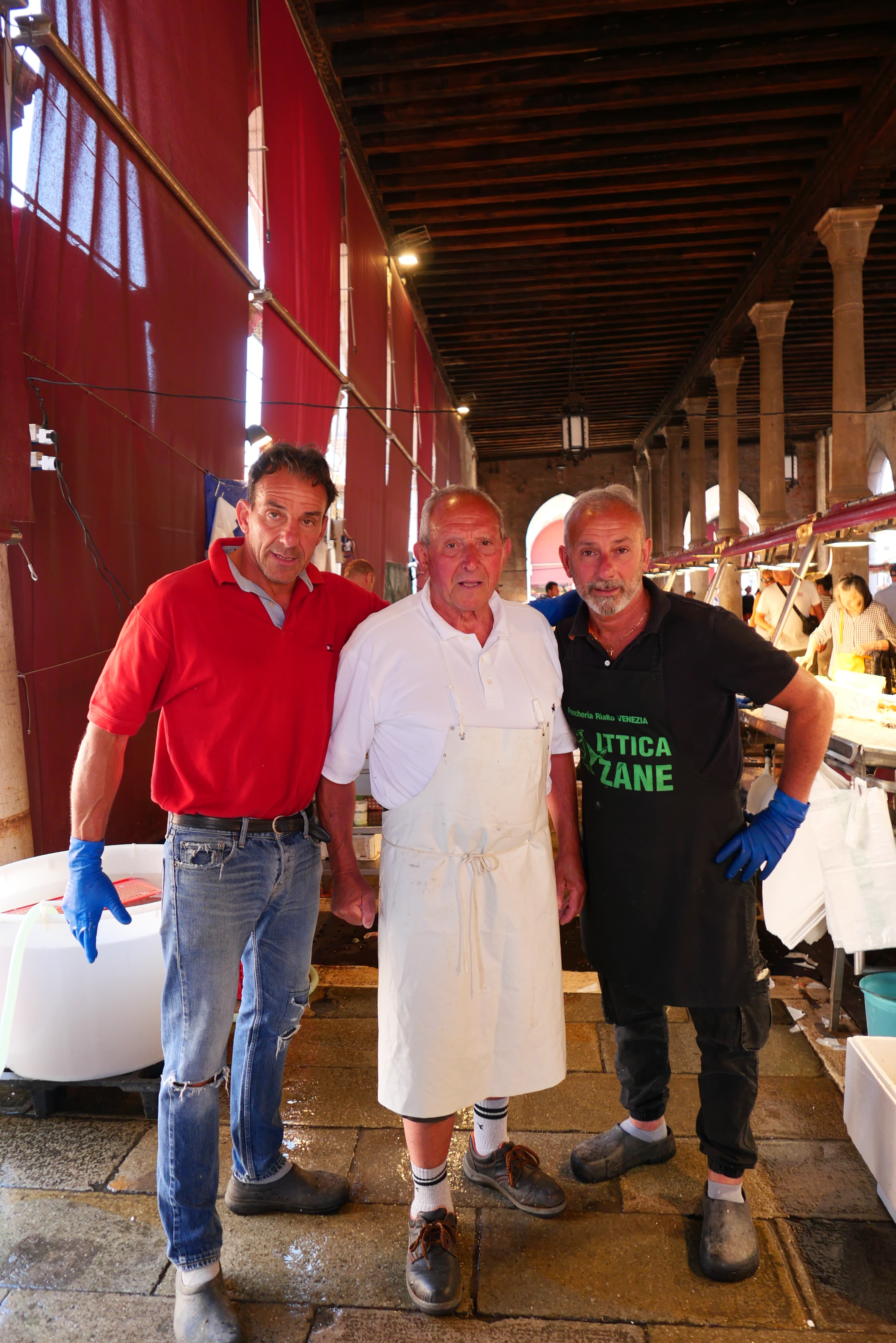Trois générations de poissonniers se tiennent côte à côte devant leur étal familial au sein du marché aux poissons historique du Rialto, à Venise